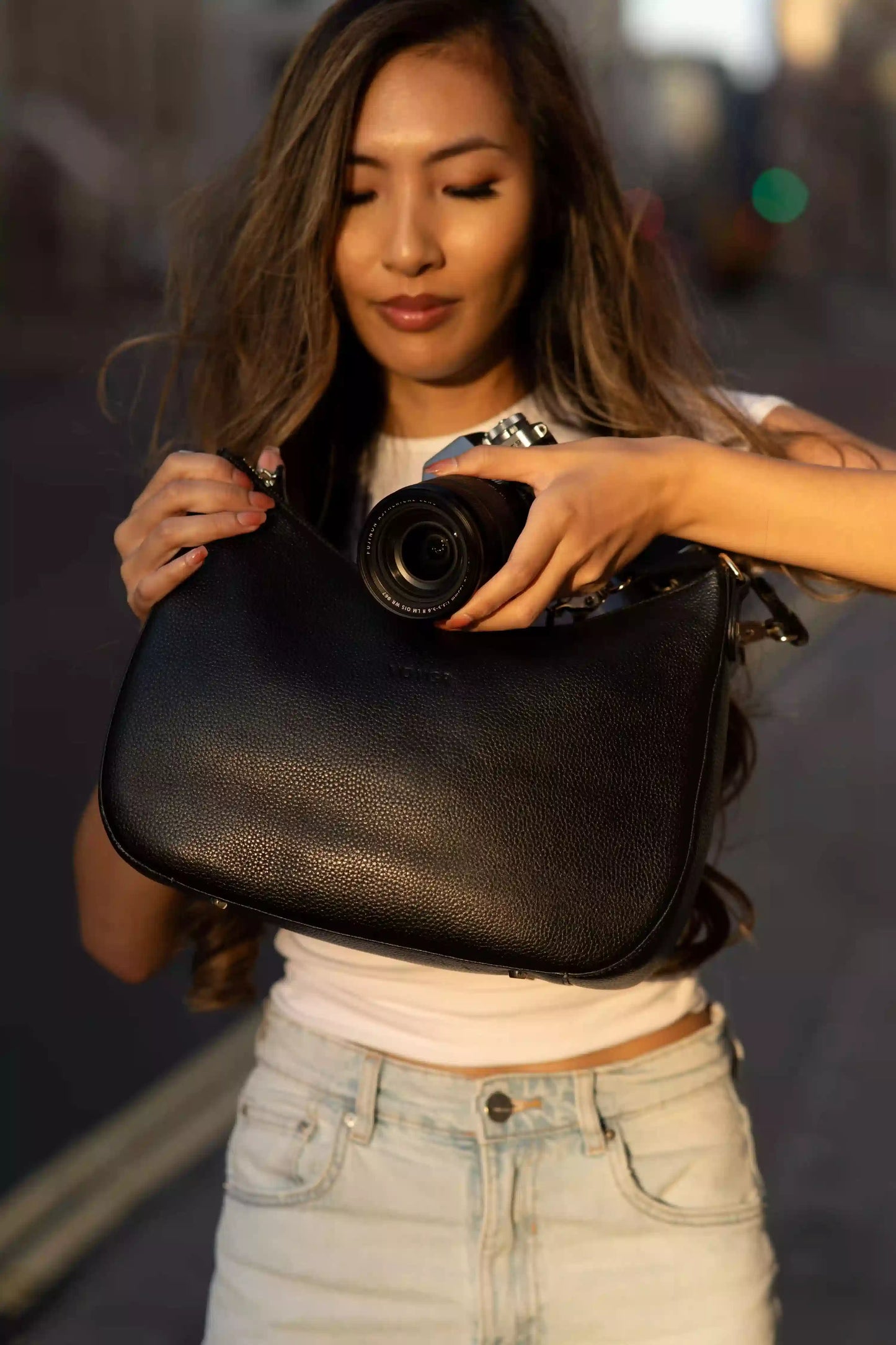 Woman holding a black leather camera bag with a blurred background