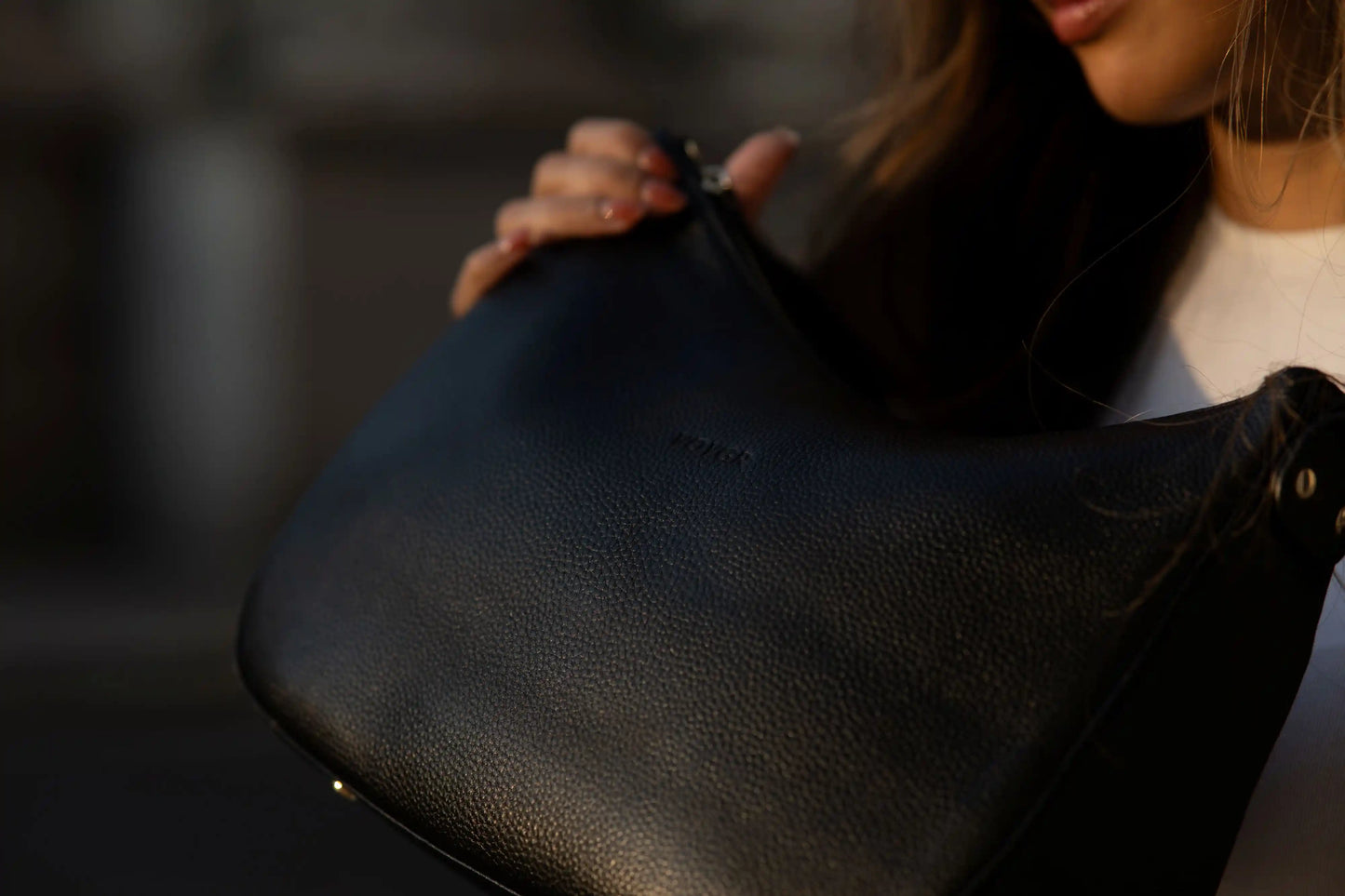 Person holding a black leather Voygr camera bag with a blurred background