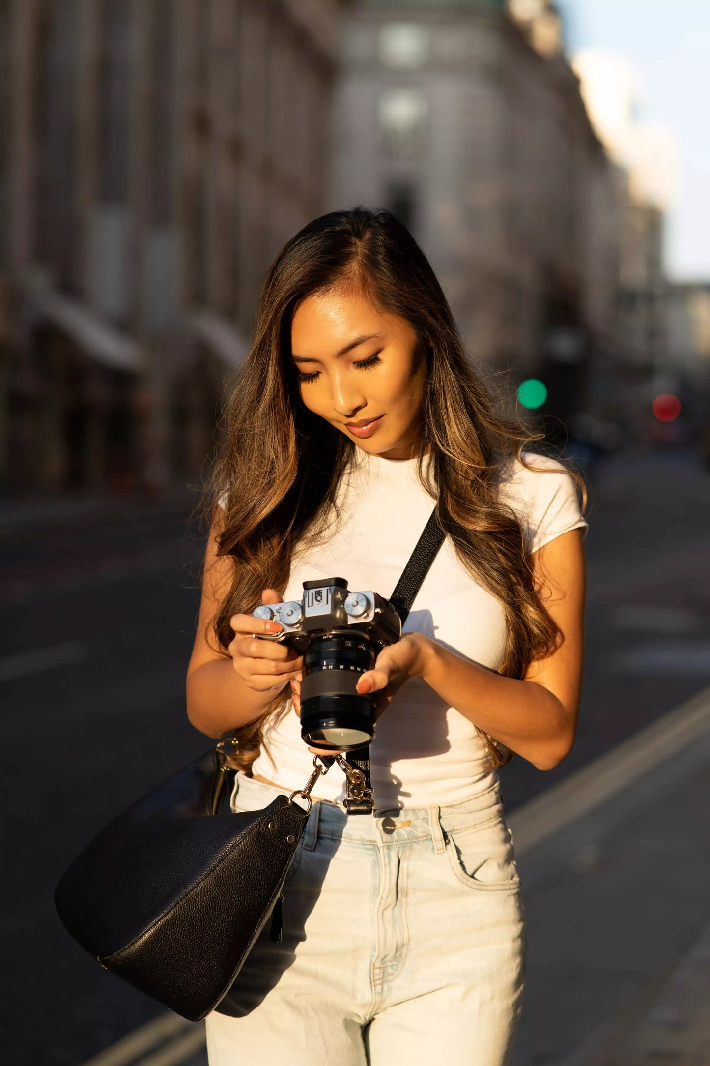 Woman holding a camera on a city street with camera bag