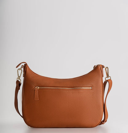 A tan pebbled leather crescent-shaped shoulder bag with a front zippered pocket and gold-tone hardware, shown against a light gray studio background.