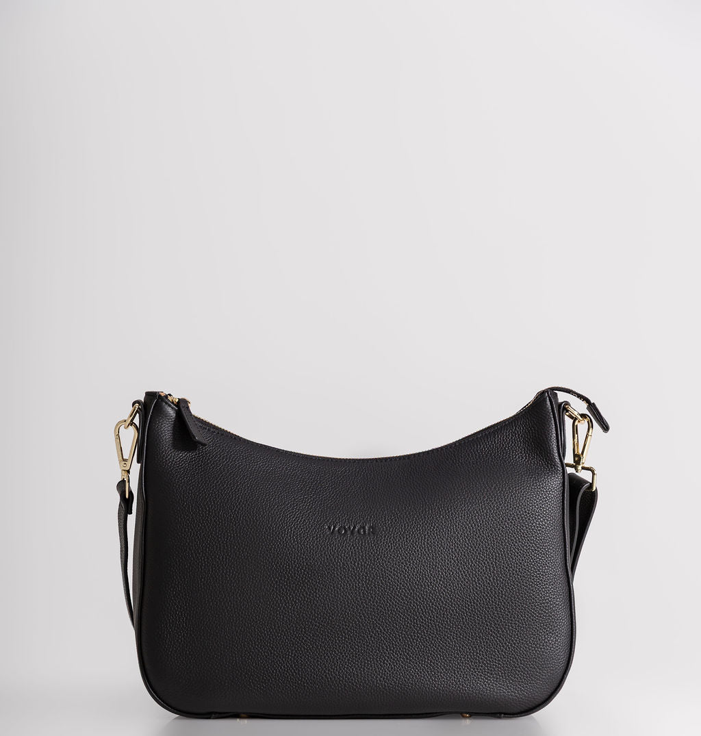 A black pebbled leather crescent-shaped shoulder bag with gold-tone hardware and a small debossed 'VOYAGE' logo on the front, set against a plain light gray background.