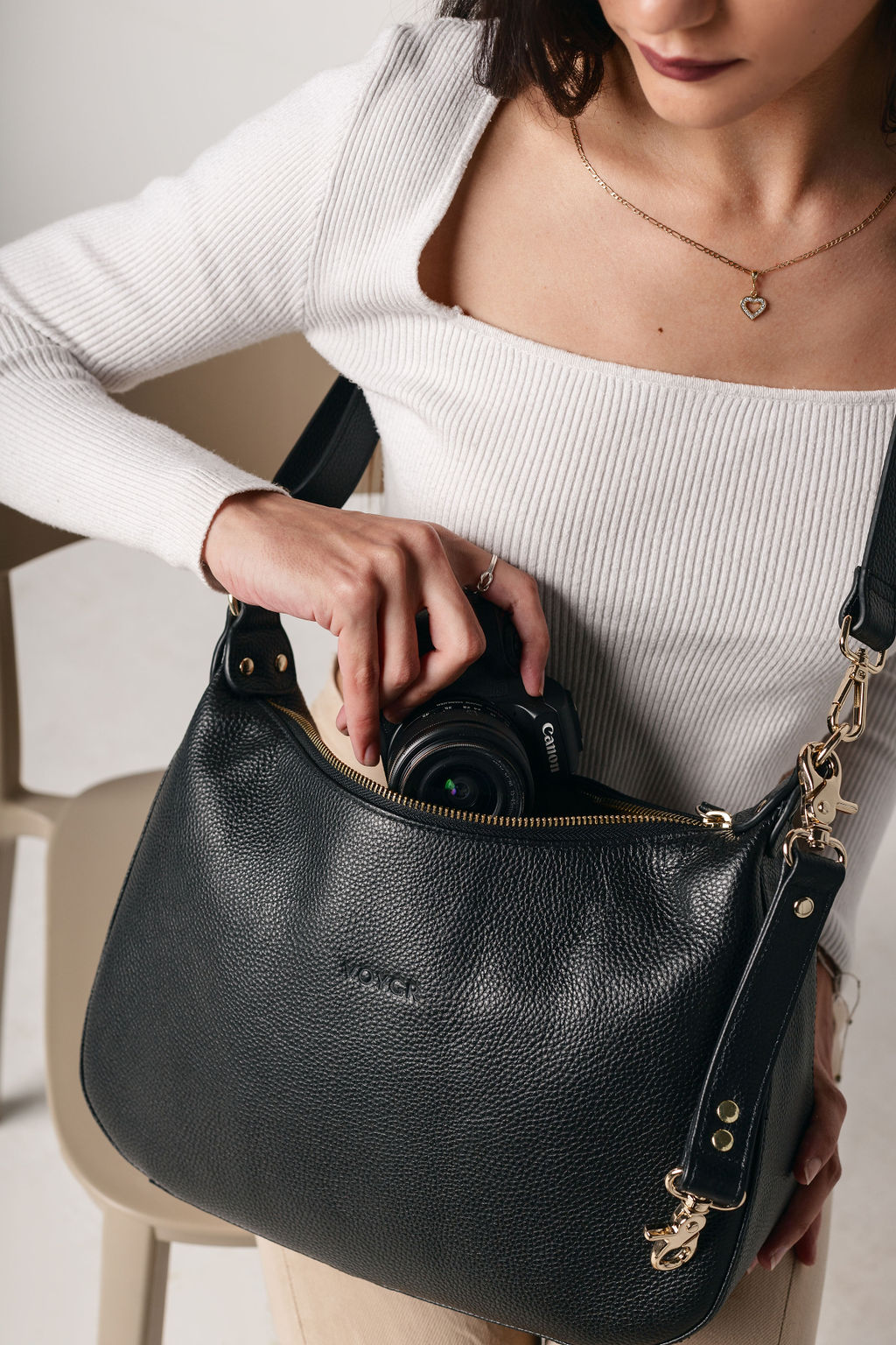 Person holding a black Voygr camera bag with a camera inside, wearing a white top.